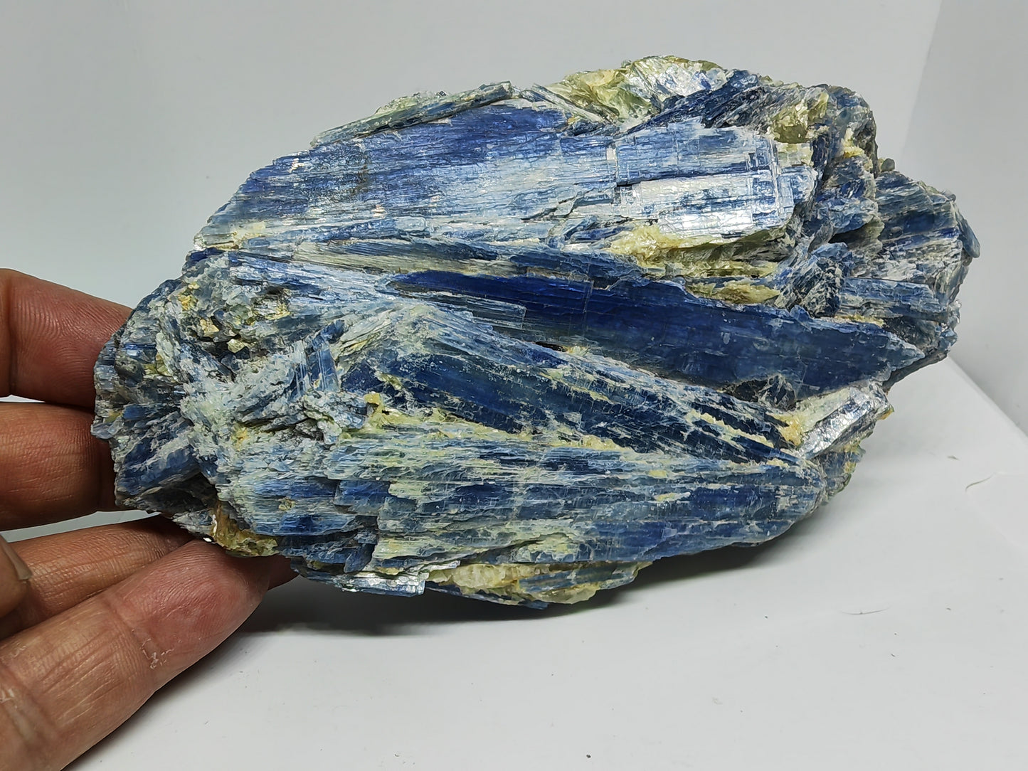 Hand holding a large blue and green mineral rock on a white surface